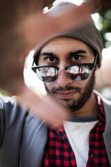 Close-up: young man in shades and cap, reflecting sunlight, urban Madrid.
