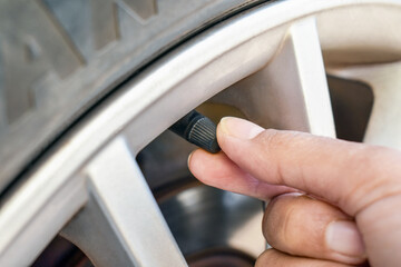 Hand checking car tyre valve cap before driving. 