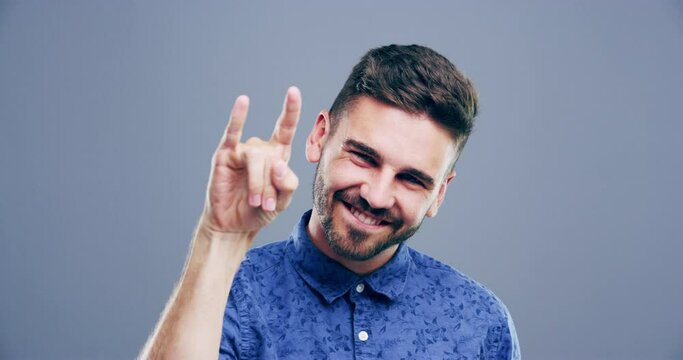 Rock, hand sign or face of happy man in studio on grey background for freedom, energy or emoji. Shaka, excited or portrait of a cool person isolated for devil horns gesture, punk or edgy attitude