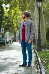 Young man in urban style, red-checkered shirt, hat, stands on sunny Madrid street.