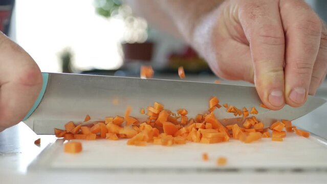 Blurred Shooting with a Man in the Kitchen Slicing with a Knife a Sweet Carrot for a Salad. Preparing a Salad with Fresh Vegetables.