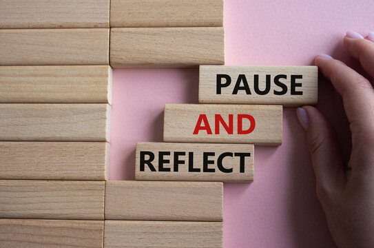 Pause and Reflect symbol. Concept words Pause and Reflect on wooden blocks. Beautiful pink background. Businessman hand. Business and Pause and Reflect concept. Copy space.