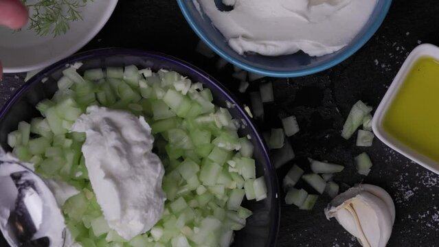 Close up footage of adding strained greek yogurt to diced fresh cucumbers for preparing traditional Bulgarian dill salad called Snejanka or Mlechna salata