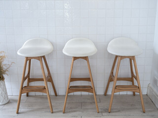 Three empty white seat wooden bar stool chairs on vintage tiles wall background, loft style cafe...