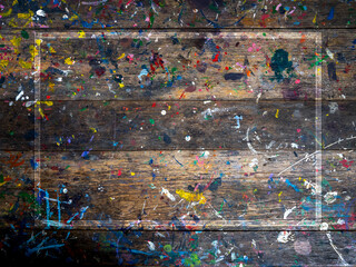 White frame on wood plank top table covered in oil or acrylic color paint splatter. Abstract texture of old rustic wooden desk background of artist studio with messy colorful color painted splash.
