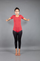 Healthy young woman in red t-shirt and black leggings doing yoga and stretching exercises isolated on grey background