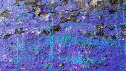 Dark purple old crumbling concrete wall with black spots and cyan paint splashed