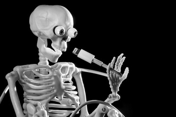 Funny skeleton toy holding a phone charging cable, he symbolizes USB Lightning connector dead for a...