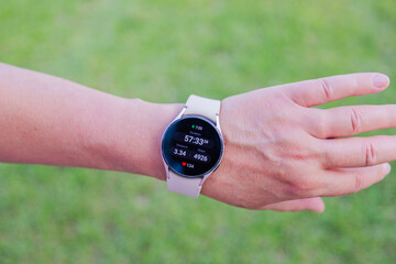 Close-up view of female hand adorned with smartwatch displaying high step count on blurred green background.