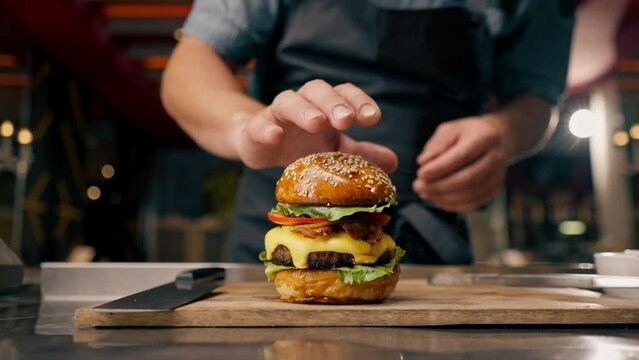 Close-up of a chef pinning a burger with beef patty with vegetables and cheese cooked in the professional kitchen of an Italian restaurant