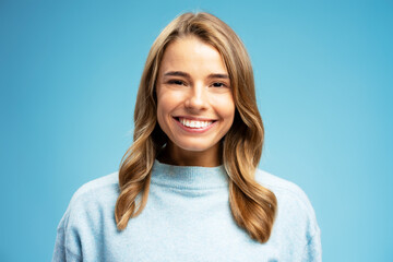 Smiling beautiful woman with silky wavy looking at camera isolated on blue background. Hair care, advertisement concept