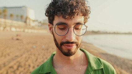Close-up of a young guy with glasses standing on the beach with his eyes closed