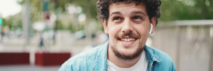 Obraz premium closeup portrait of young bearded man in denim shirt posing and smiling at camera on modern cityscape background.