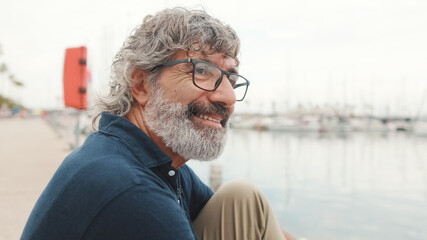 Close-up of an middle aged man sitting on pier in marina and listening attentively to someone on...