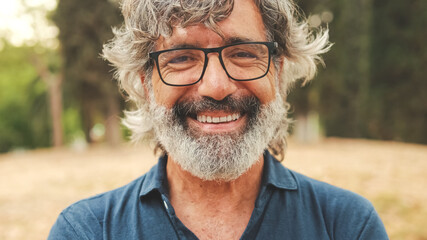 Close-up of retired man with glasses crossing his arms and looking at the camera with smile while...