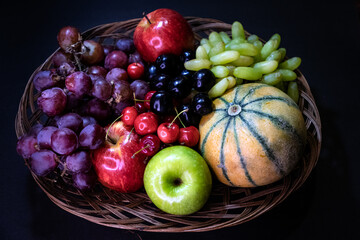 Assortment of juicy fruits red apple, green apple, red grapes, green grapes and musk melon on the fruit basket against dark background