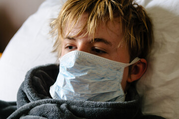 Teenage boy lying in bed wearing a mask