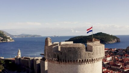 Drone flies over historic old town Dubrovnik Croatia capturing a beautiful aerial shot of castle wall lookout tower with flapping flag in the sunlight over the Adriatic Sea - Powered by Adobe