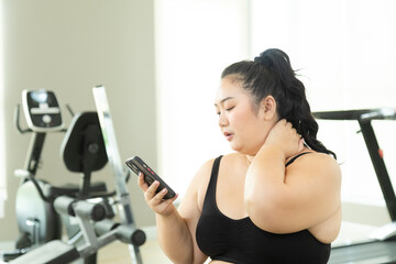 Happy Asian overweight woman use smartphone looking video online relaxing in fitness club, chubby...