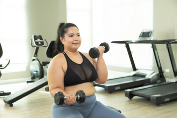 Happy Asian overweight woman lifting up dumbbell two arms in fitness club, healthy strong chubby females wearing sportswear exercise building muscles, happy curvy girls in weight loss workout program