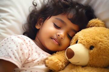 Little Indian girl with dark hair in shirt sleeps sweetly in company of best friend teddy bear seeing pleasant dreams. Little girl has sweet dreams in bed with favorite toy small teddy bear - obrazy, fototapety, plakaty