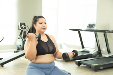 Fototapeta na wymiar Happy Asian overweight woman lifting up dumbbell two arms in fitness club, healthy strong chubby females wearing sportswear exercise building muscles, happy curvy girls in weight loss workout program