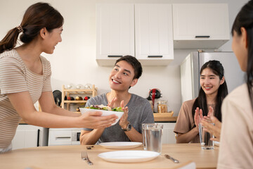 Happy Asian friends lunching with healthy food home- Young people having fun eating meal and drinking water for lunch.