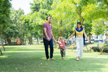 Cute little boy having fun jumping to the sky holding hands of mother and father bonding relationship in park summer vacation, Caucasian family mom, dad, and son relaxing playing together outdoors