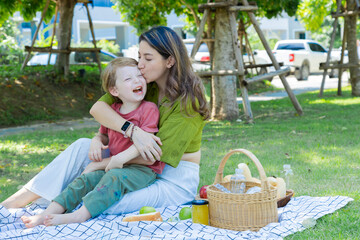 ็Hispanic  little boy son sitting on mom lap, mother kissing and embracing happy kid laughing with female motherhood relaxing summer holiday vacation, Caucasian family outdoor activities lifestyle