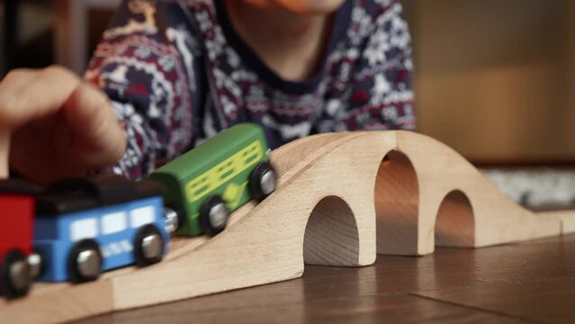 Closeup of boy in pajamas lying on floor and playing with toy wooden train and railroad