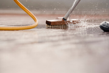 Detail of a scrubbing brush during spring cleaning of a wooden terrace floor with sparkling water...