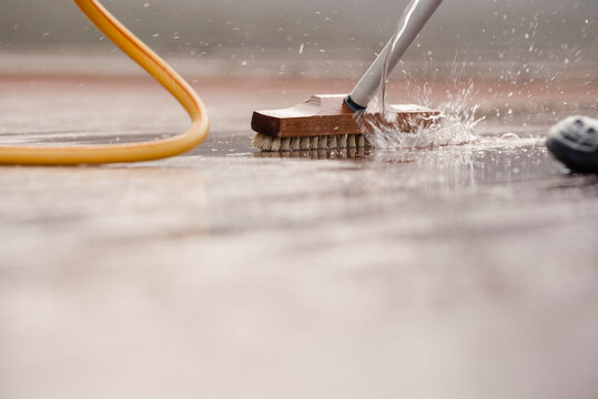 Detail of a scrubbing brush during spring cleaning of a wooden terrace floor with sparkling water with space for text