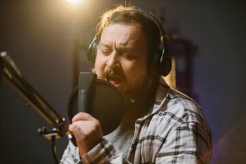 Portrait of a radio presenter or blogger in a home studio. A man in headphones speaks expressively...