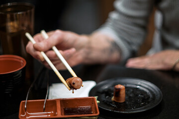 Fototapeta na wymiar Japanese Yakiniku BBQ sauce drips from a grilled sausage held between the tips of two chopsticks