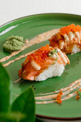 Sushi nigiri with a grilled salmon and caviar. Sushi rolls on green plate with wasabi and ginger. Top view with copy space. Traditional japanese dish.