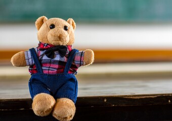 Closeup shot of an adorable fluffy brown teddy bear in cute overalls on a wooden surface