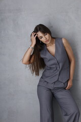 Sexy luxury woman in grey masculine costume, grey wall background. Beautiful brunette girl standing ans smiling. Portrait of lady in great shape. Big lips and stylish woman model