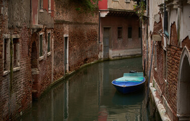 Fototapeta na wymiar Small boat in Venetian canal. Old houses built on the channel.