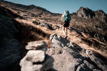 Frau-Bergsteiger mit grünem Rucksack steigt in den Alpenpfad hinauf in braunen Farben der Umgebung
