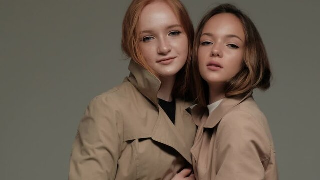 Two stylish models in a trench coat in the studio on a gray background.
