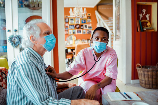Female caregiver examining senior patient with stethoscope at home