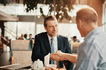 Two businessmen shaking hands while sitting in cafe