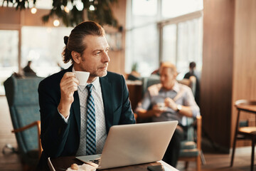 Businessman sitting in cafe drinking coffee working on laptop