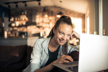 Smiling young woman sitting on couch using laptop at home