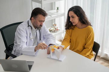 Fototapeta premium Male doctor talking to woman about illness in clinic. Caucasian doctor to check up health female in examination hospital room. Healthcare and medical concept.