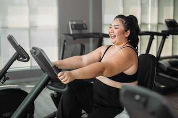 Plus size Asian woman exercises in gym. Beautiful overweight woman in sportswear doing cardio...