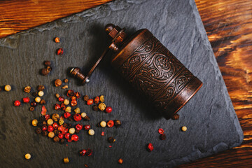 Old metal pepper and spice mill on slate tiles, on a wooden background.