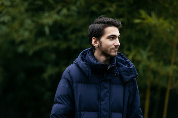 Profile portrait of a handsome young man in park, wear in warm clothes, tree background.