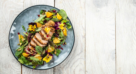 Salad with baked duck, green salad mix and oranges on a light background. Long banner format. top view. copy space for text - obrazy, fototapety, plakaty
