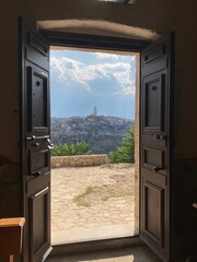 Vertical shot of an open wooden door with a view of a hill with buildings on a sunny day